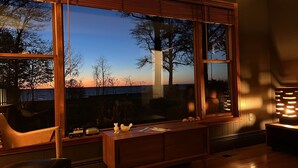 Een moderne woonkamer met een groot raam met uitzicht op een wateroppervlak, een houten bureau en een comfortabele zithoek.