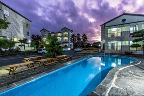 Una piscina con mesas de picnic, rodeada de edificios de piedra con numerosas ventanas y balcones.