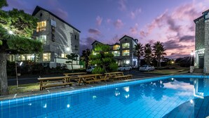 Una piscina con cubierta de madera y bancos, rodeada de edificios con amplias ventanas y fachada de piedra.