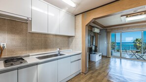 Una cocina moderna con armarios blancos, un lavamanos de acero inoxidable y una estufa integrada. Tiene piso de madera y un amplio ventanal con vistas al océano.