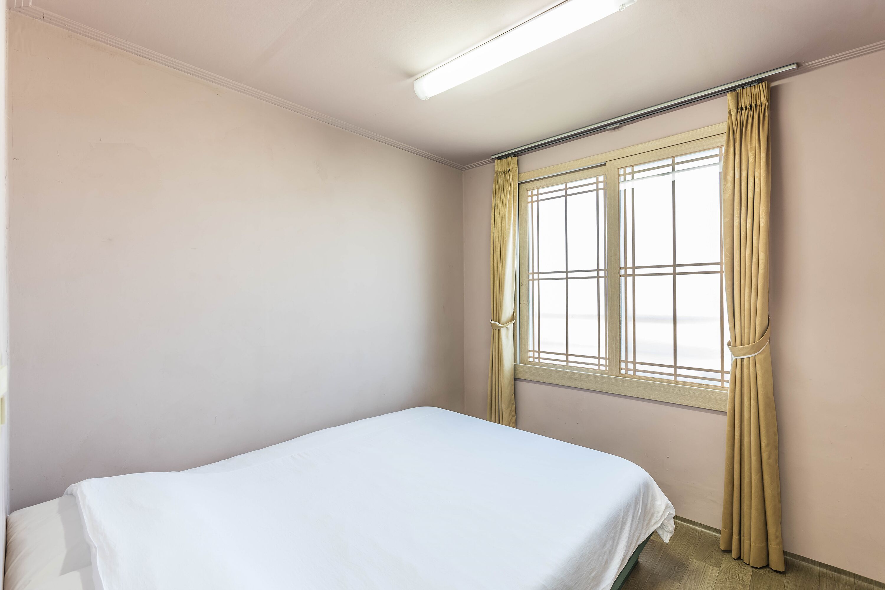A room with a bed, a window with curtains, and a ceiling light.