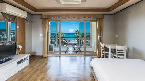 Habitación de hotel con balcón, televisión, cama y zona de comedor.