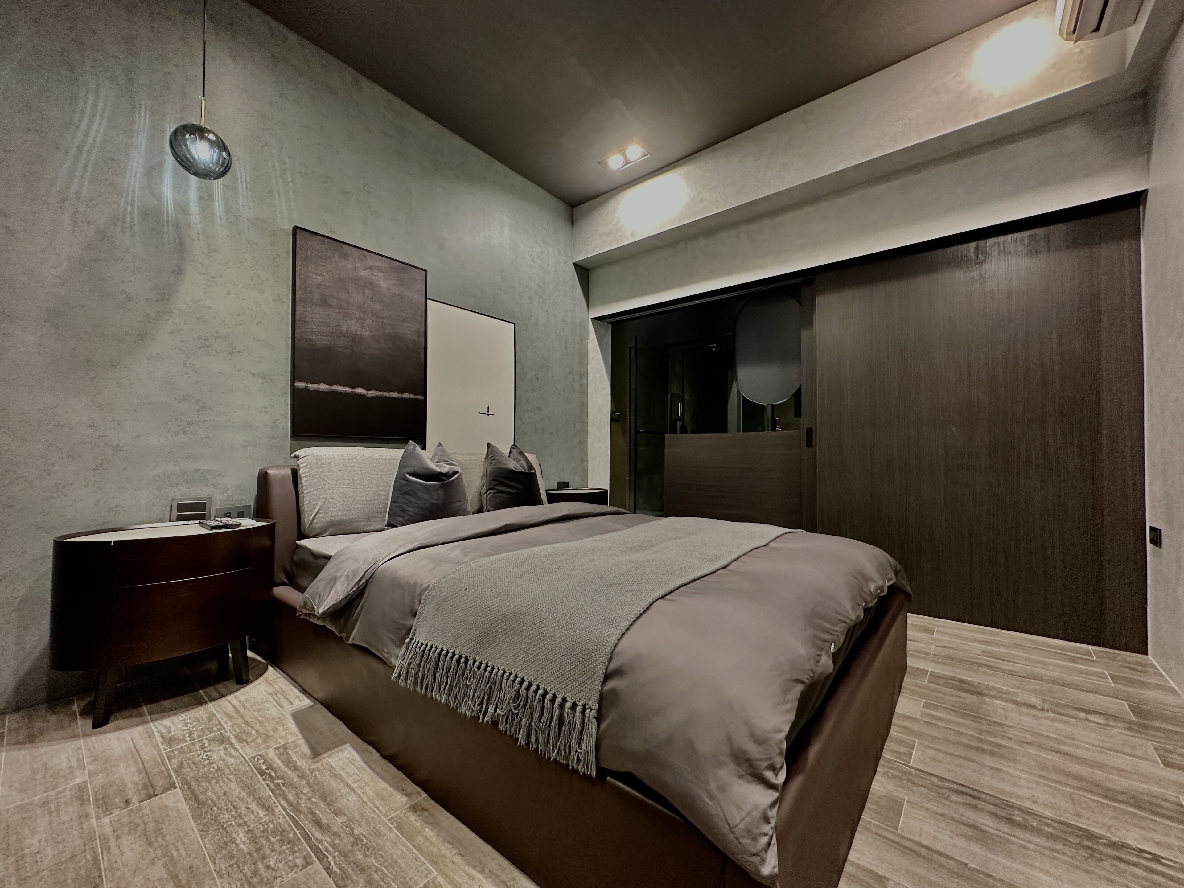 A modern bedroom with a large bed, a nightstand, a wall-mounted lamp, and a wardrobe.