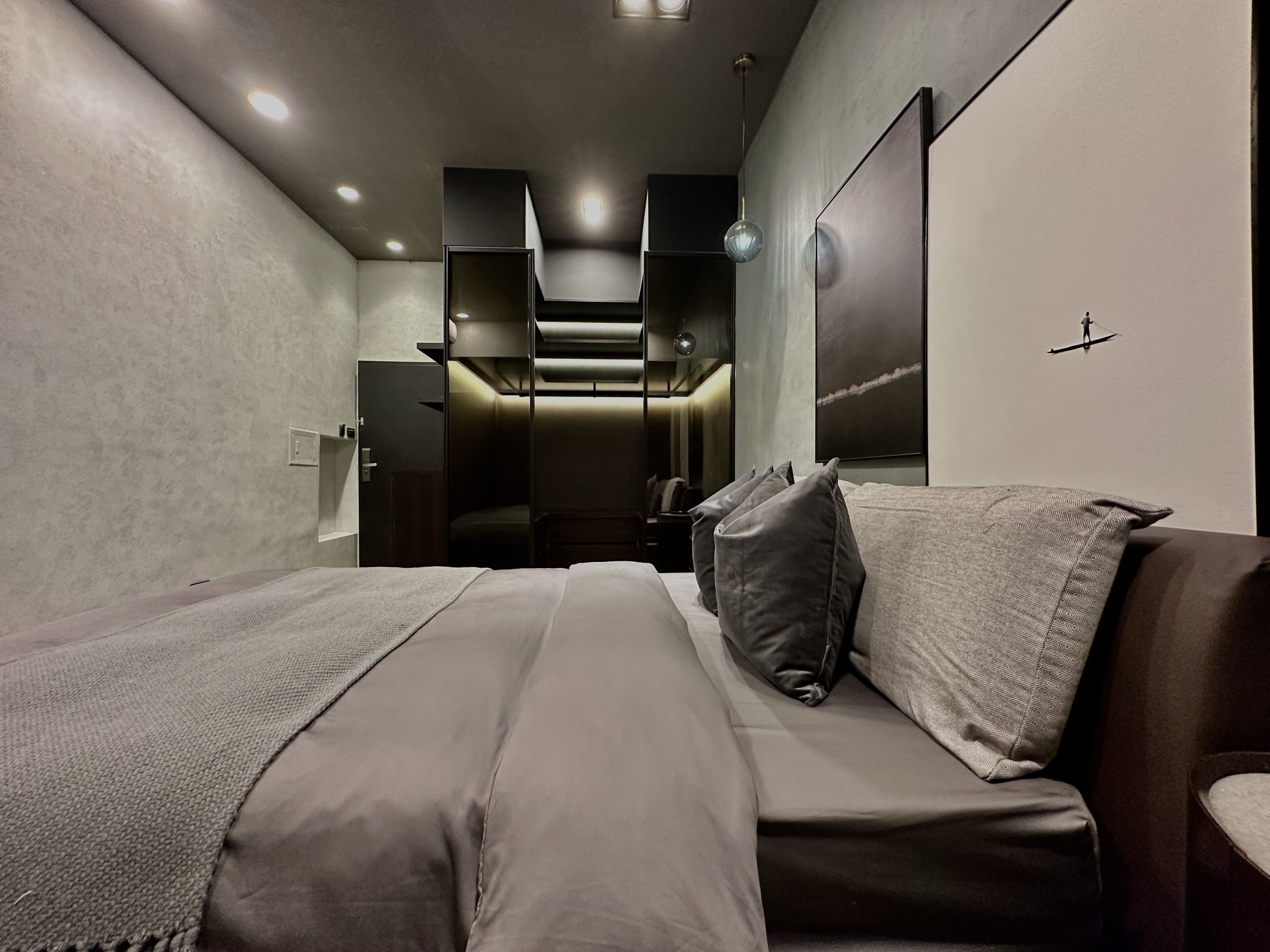 A modern hotel room with a large bed, a wardrobe, and a small seating area.