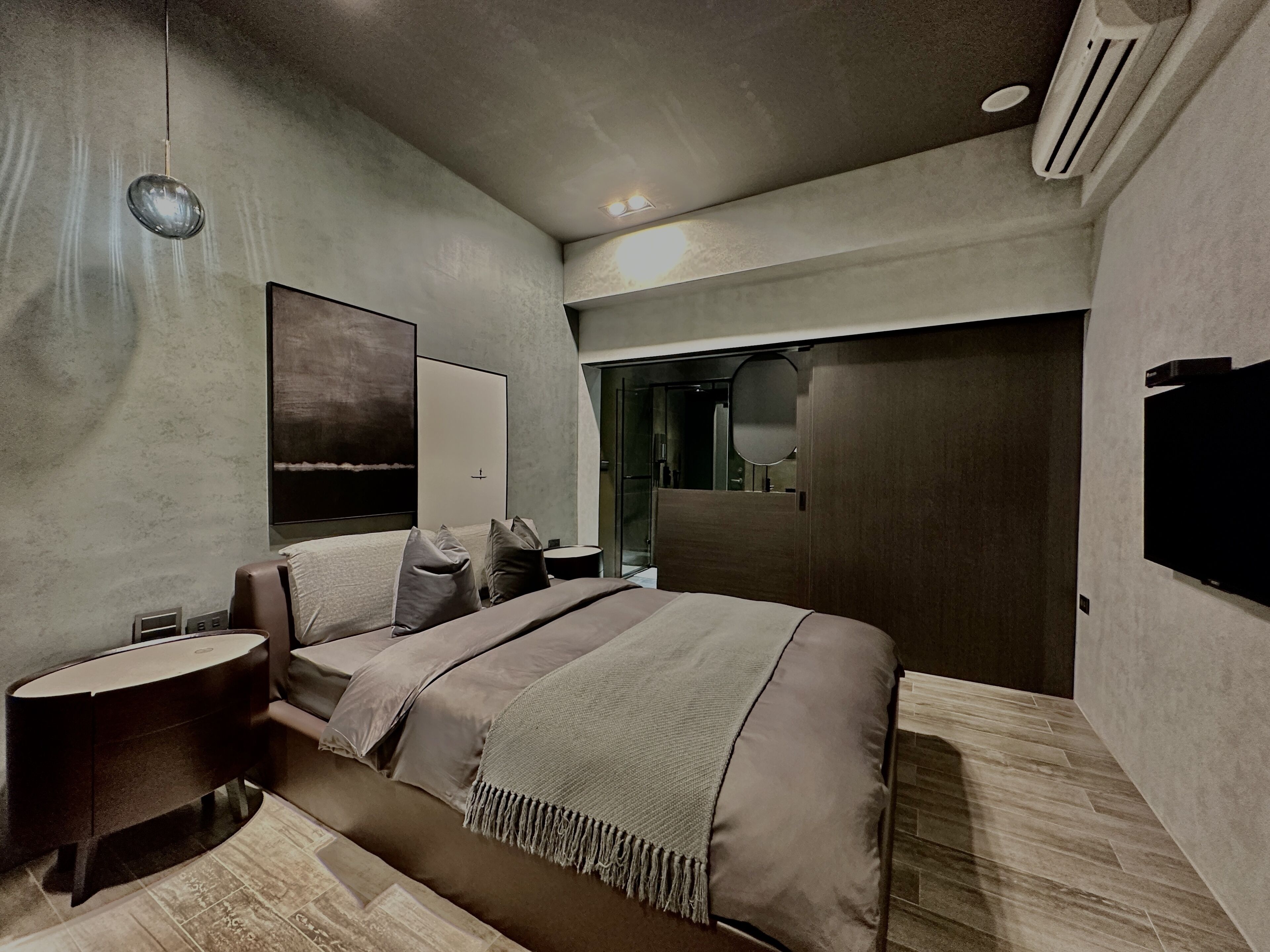 Un dormitorio moderno con una cama grande, mesitas de noche, un espejo y un televisor en la pared.
