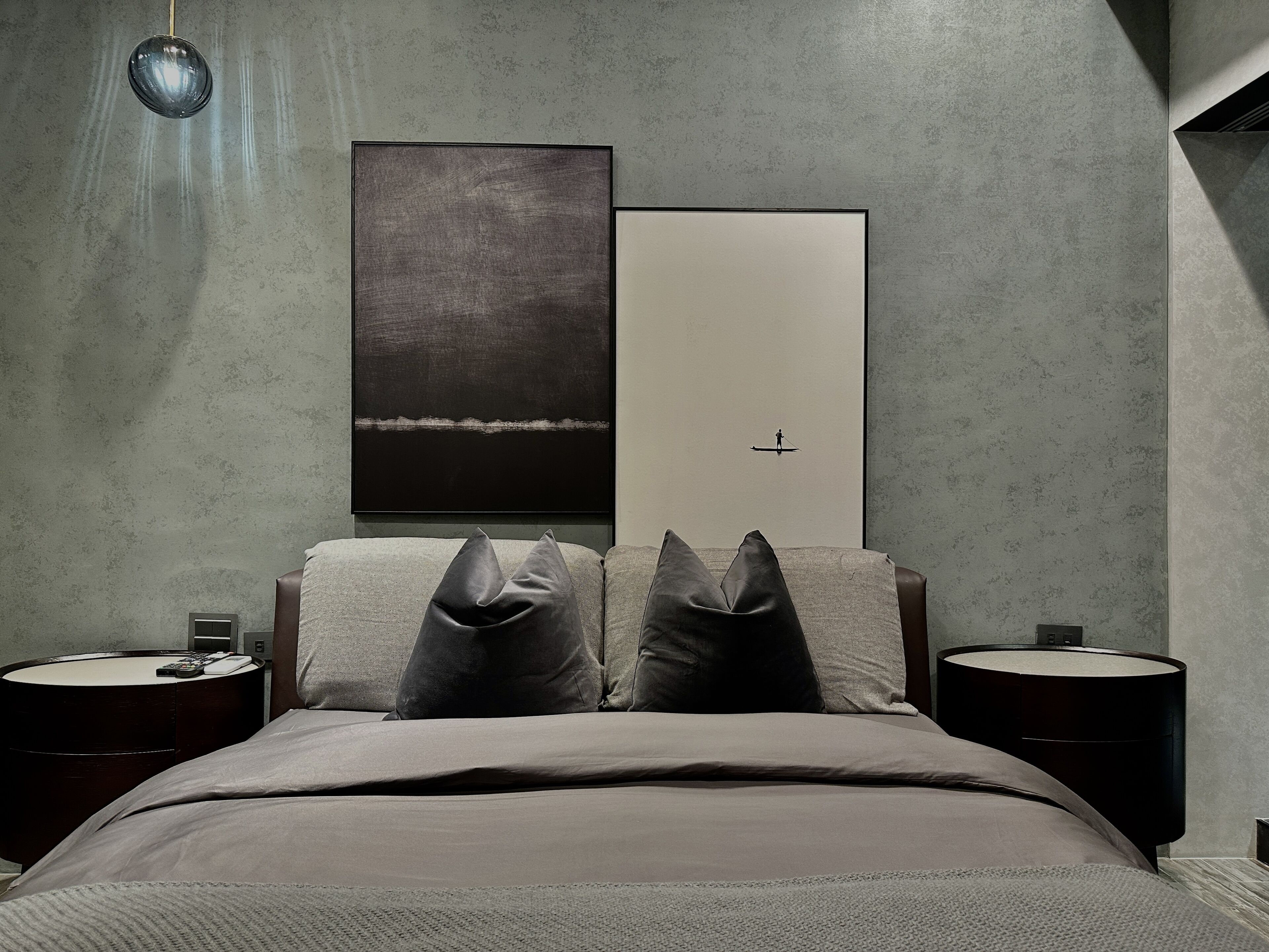 A modern bedroom with a large bed, two nightstands, a wall-mounted lamp, and two framed artworks.