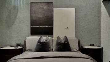 A modern bedroom with a large bed, two nightstands, a wall-mounted lamp, and two framed artworks.