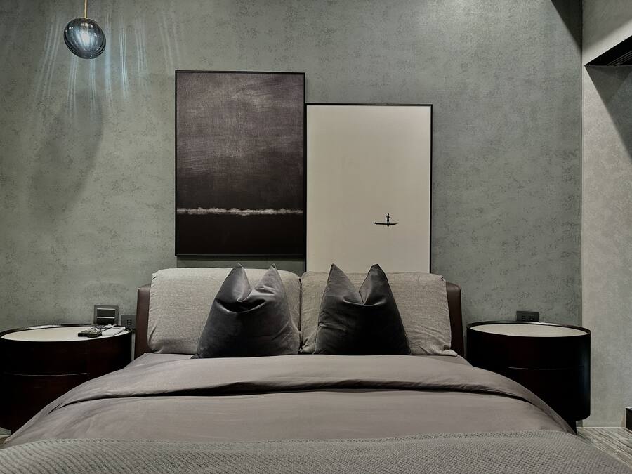 A modern bedroom with a large bed, two nightstands, a wall-mounted lamp, and two framed artworks.