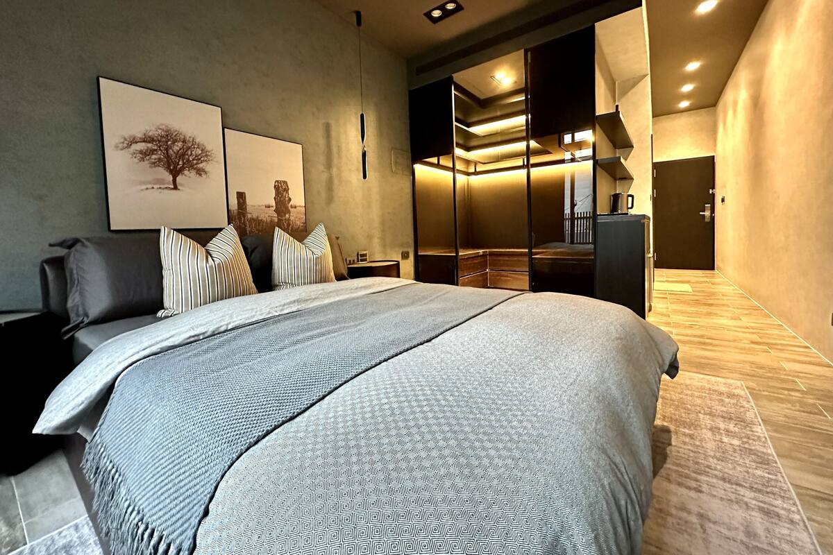 Ein modernes Schlafzimmer mit einem großen Bett, einer dunklen Couch und einem begehbaren Kleiderschrank mit Schiebetüren.