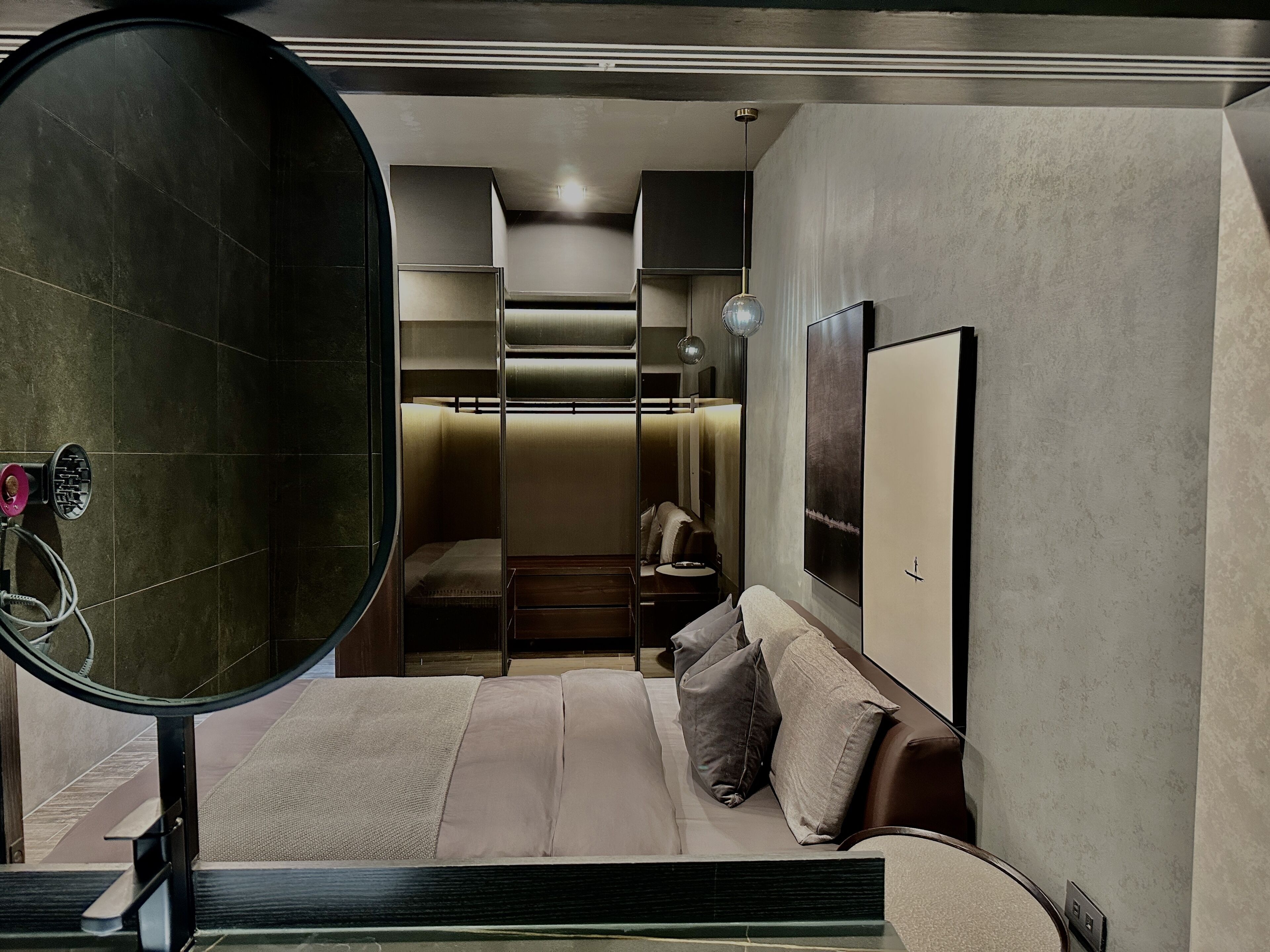 A modern bedroom with a large mirror, a bed with multiple pillows, a nightstand, and a wardrobe.