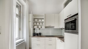 A compact kitchen with white cabinetry, a built-in oven, and a window with curtains.
