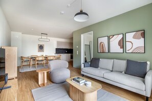 Ein modernes Wohnzimmer mit einem grauen Sofa, einem Esstisch mit Stühlen und einer Küche im Hintergrund.