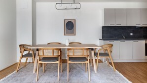 Eine moderne Küche mit weißen Schränken, einer schwarzen Arbeitsplatte und einem Essbereich mit Holztisch und Korbstühlen.