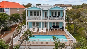 Une maison à deux étages avec une piscine, des balustrades blanches et un balcon agrémenté de mobilier d’extérieur.