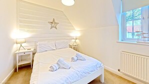 Une chambre avec un lit blanc, deux tables de chevet avec des lampes, une décoration en forme d’étoile sur le mur et une fenêtre donnant sur des immeubles.