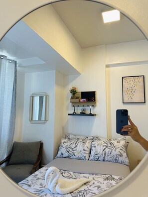 Ein Schlafzimmer mit einem Bett, einem Sessel, einem Spiegel, einem Regal mit Dekoration und einem gerahmten Bild an der Wand.