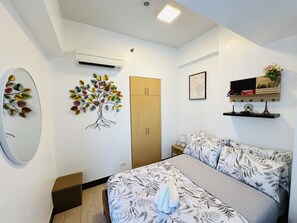 Een slaapkamer met een bed, een kledingkast, een wandairconditioner, een decoratieve plant, een ingelijste foto en een plank met spullen.