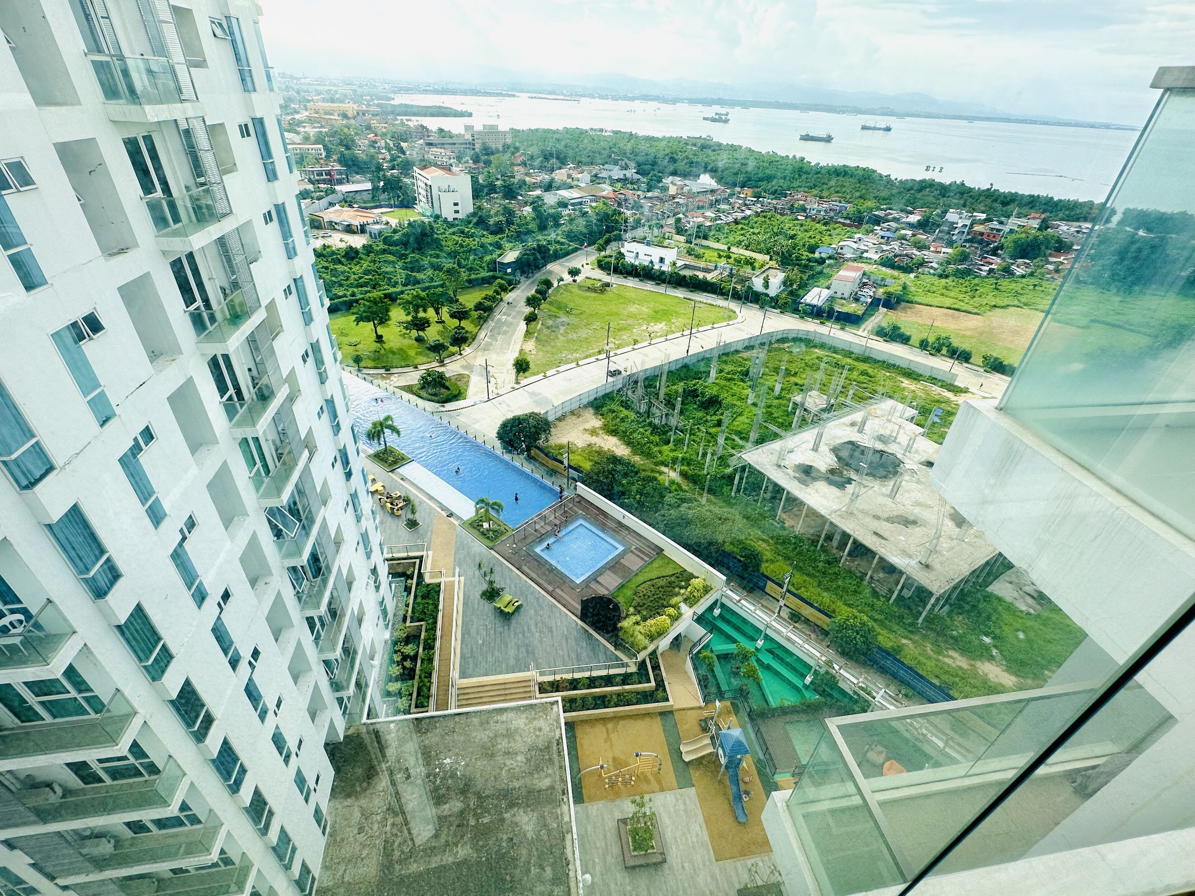 A high-rise building with a rooftop pool and a view of a cityscape including a river and distant mountains.