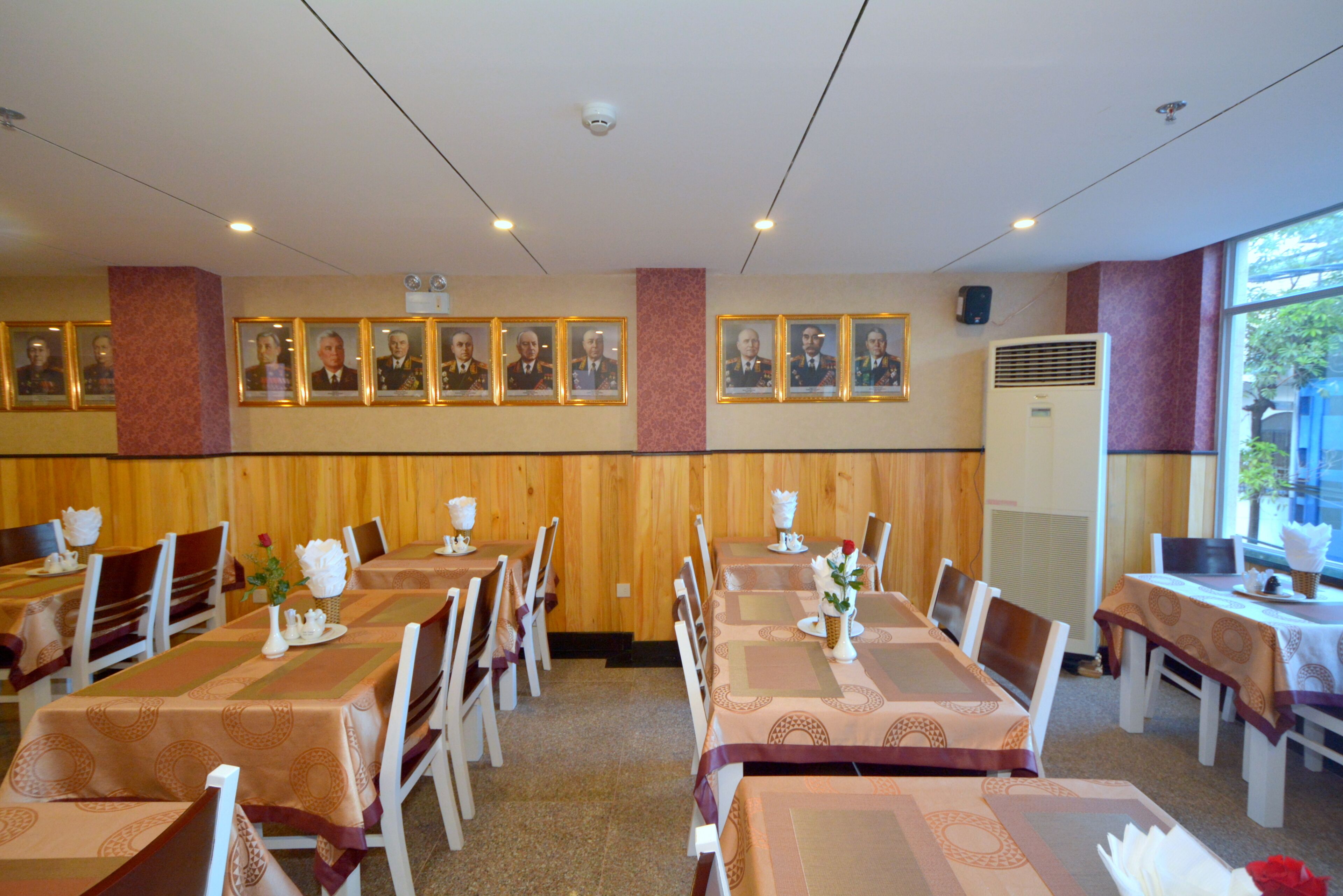 Un restaurante con varias mesas, sillas, retratos enmarcados en la pared y un ventanal con vistas al exterior.