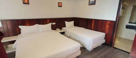A hotel room with two beds, a wooden headboard, a bedside table with a phone, and a small wall-mounted light fixture.