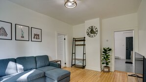 A living room with a sectional sofa, a wall clock, framed artwork, and a potted plant. - Modern Hastings-On-Hudson Home Near River! (Hastings-On-Hudson)