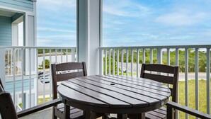 Ein Balkon mit rundem Tisch und zwei Stühlen, mit Blick auf eine Straße mit geparkten Autos und Grünflächen.