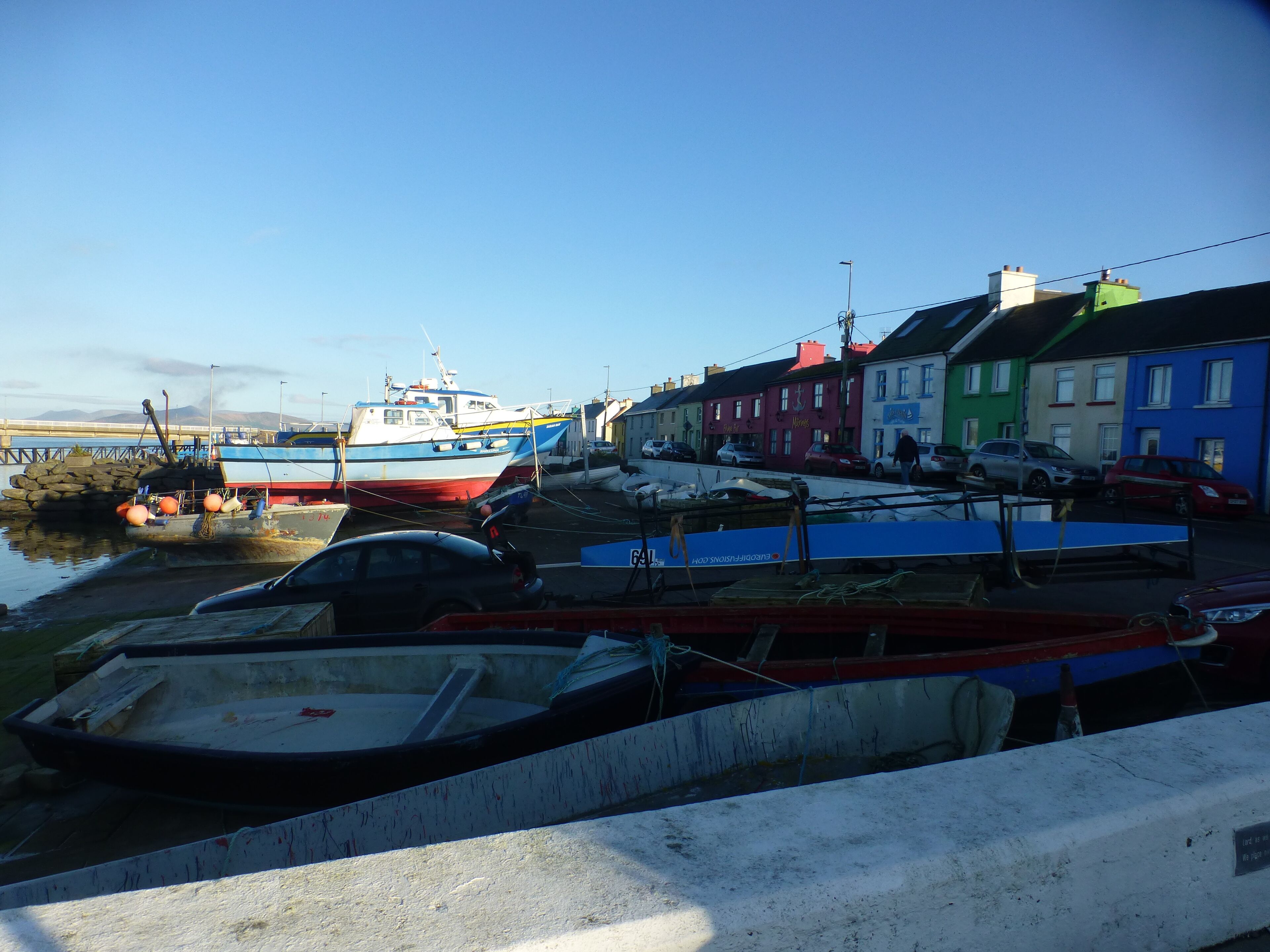 A harbor with boats docked, a bridge in the background, and colorful buildings along the shore.