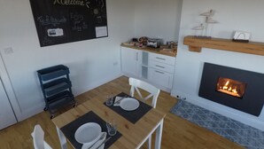 A dining area with a wooden table set for two, a blackboard with a welcome message, a kitchen area with a toaster and a shelf, and a fireplace. - Triple room with ensuite bathroom (Portmagee)