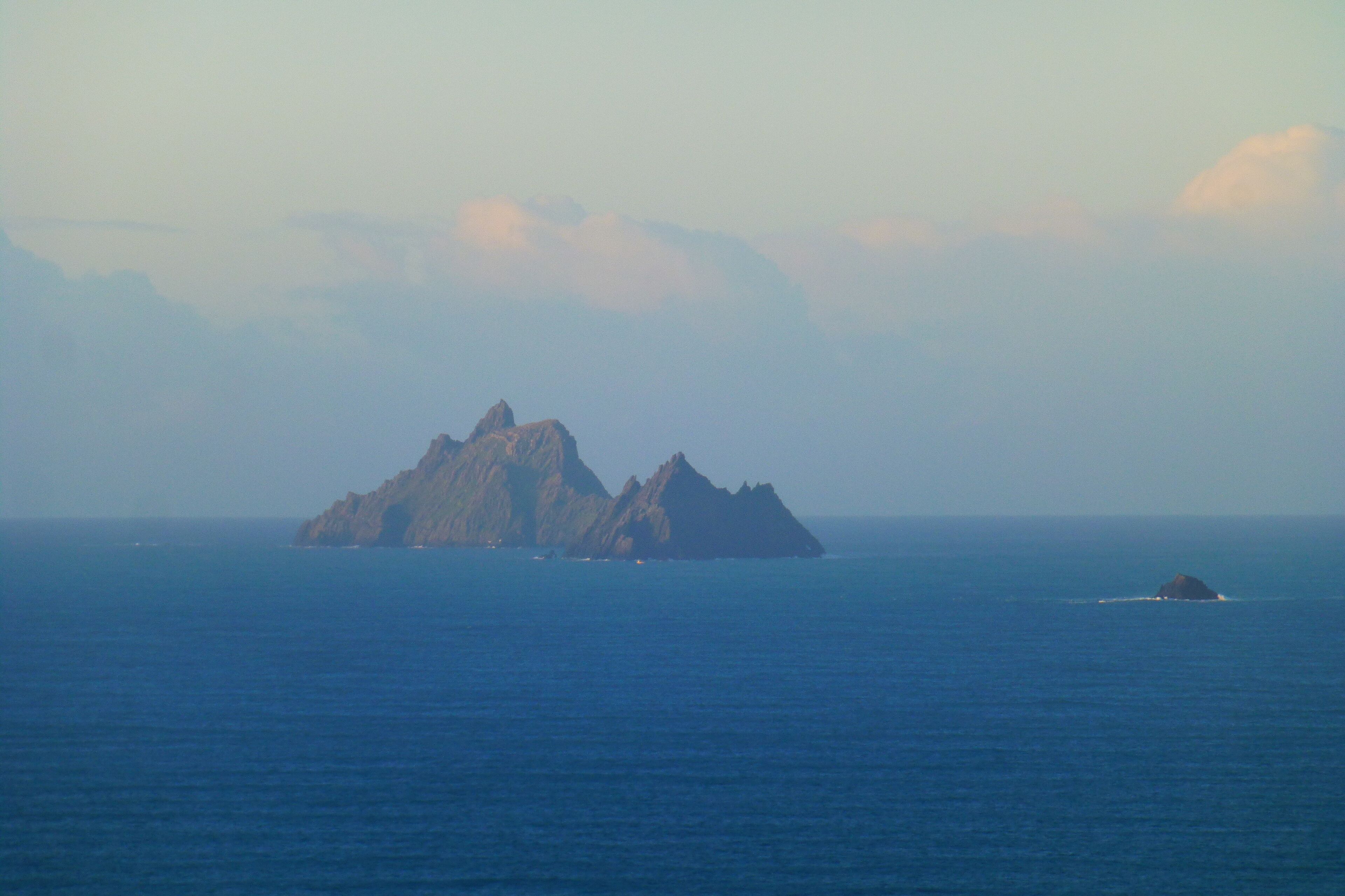 A coastal landscape with a prominent rocky island and a smaller island in the distance.