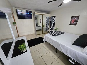Habitación de hotel con cama, televisor montado en la pared, espejo y una pequeña planta en maceta.