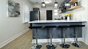 Cocina moderna con encimera de mármol, taburetes negros, lámparas colgantes y refrigerador negro.
