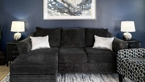 Una habitación azul oscuro con un sofá gris, dos mesitas auxiliares a juego y un cuadro abstracto enmarcado en la pared.