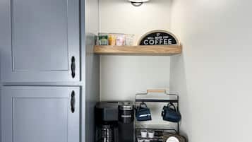 A kitchen area with a coffee maker, a coffee mug rack, and a sign that says "Our Little Coffee Bar."