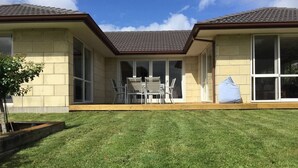 A two-story house with a patio area and a lawn. - Pacific Vistas (Athenree)