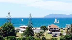 A coastal view with a sailboat, buildings, and greenery. - Pacific Vistas (Athenree)