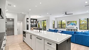 Een moderne keuken met een centraal eiland, witte kastjes en een blauwe bank in de woonkamer.