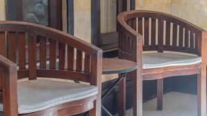 Dos sillas de madera con asientos y respaldos acolchados, ubicadas sobre un suelo de baldosas cerca de un vidrio con una pared de piedra al fondo.