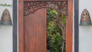 Una puerta de madera con elaborados grabados, que da a un sendero rodeado de exuberante vegetación.