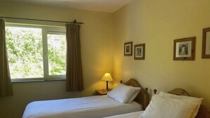 A room with two beds, a window with curtains, a lamp, and framed pictures on the wall. - Sunshine Heights by Interhome (Kenmare)