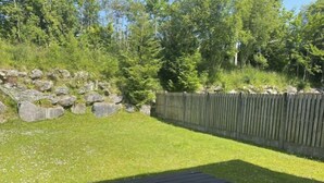 A grassy backyard with a wooden fence, a stone wall, and a picnic table. - Sunshine Heights by Interhome (Kenmare)