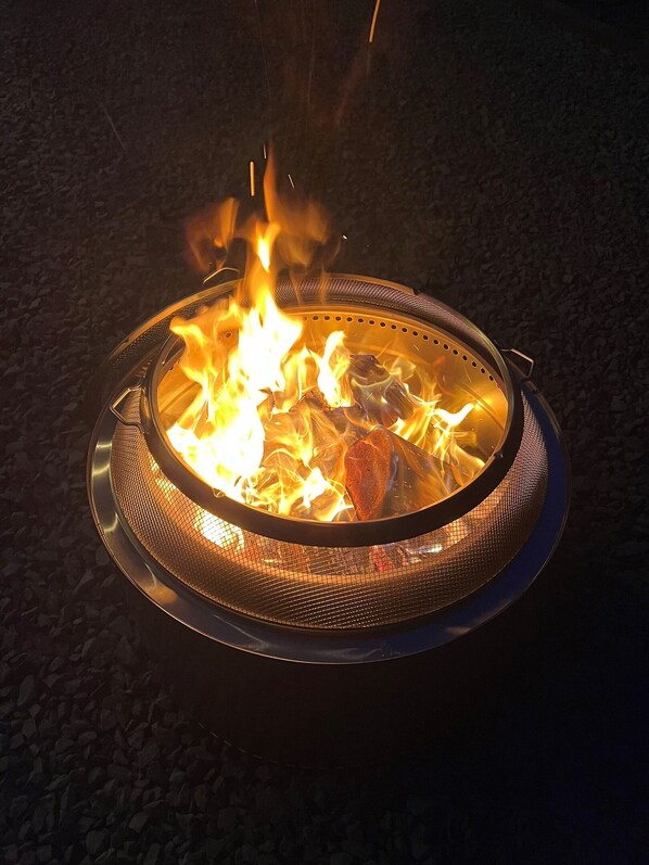 A circular metal fire pit with a mesh cover, surrounded by gravel.