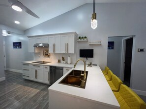 A modern kitchen with white cabinets, a built-in oven, and a large island with a sink. There is a yellow sofa and a flat-screen TV mounted on the wall. - J&K Dream Home in Sarasota near of Siesta Key. Enjoy our modern, renovated house (Sarasota)