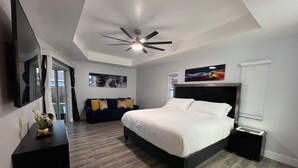 Un dormitorio moderno con una cama, un ventilador de techo, un sofá de color oscuro y un cuadro en la pared.