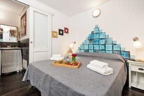 A neatly made bed with a tray of breakfast items, a bedside table with a lamp, and a decorative blue mosaic on the wall.