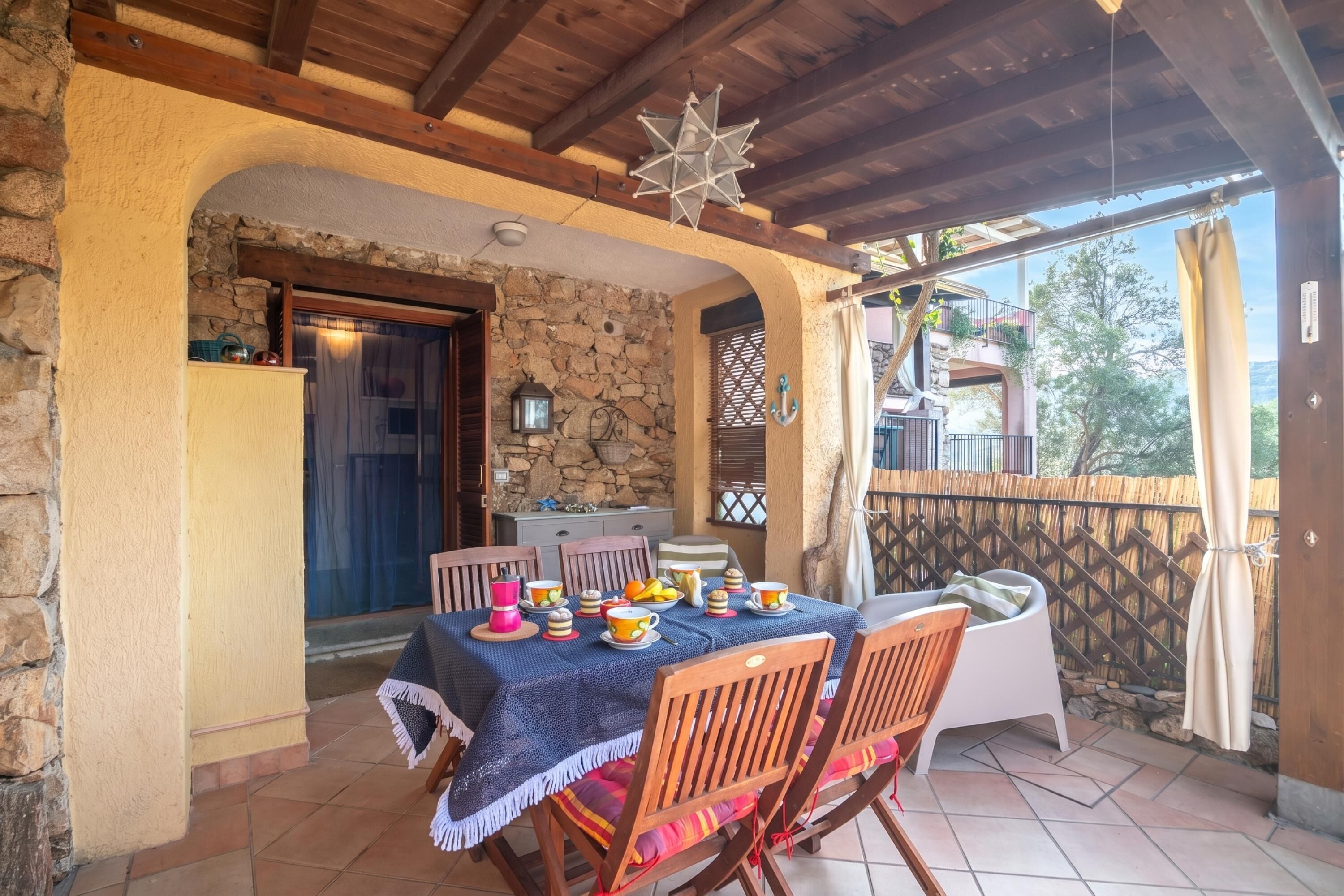 Un patio cubierto con una mesa lista para comer, paredes de piedra y techo de madera.
