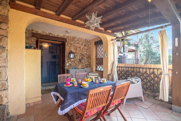 Un portico coperto con un tavolo apparecchiato per mangiare, pareti in pietra e un soffitto in legno.
