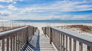 Ein hölzerner Steg führt zu einem Strand unter blauem Himmel.