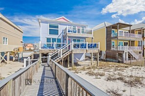 A beachfront property with a wooden boardwalk leading to a two-story building with balconies and a covered area.