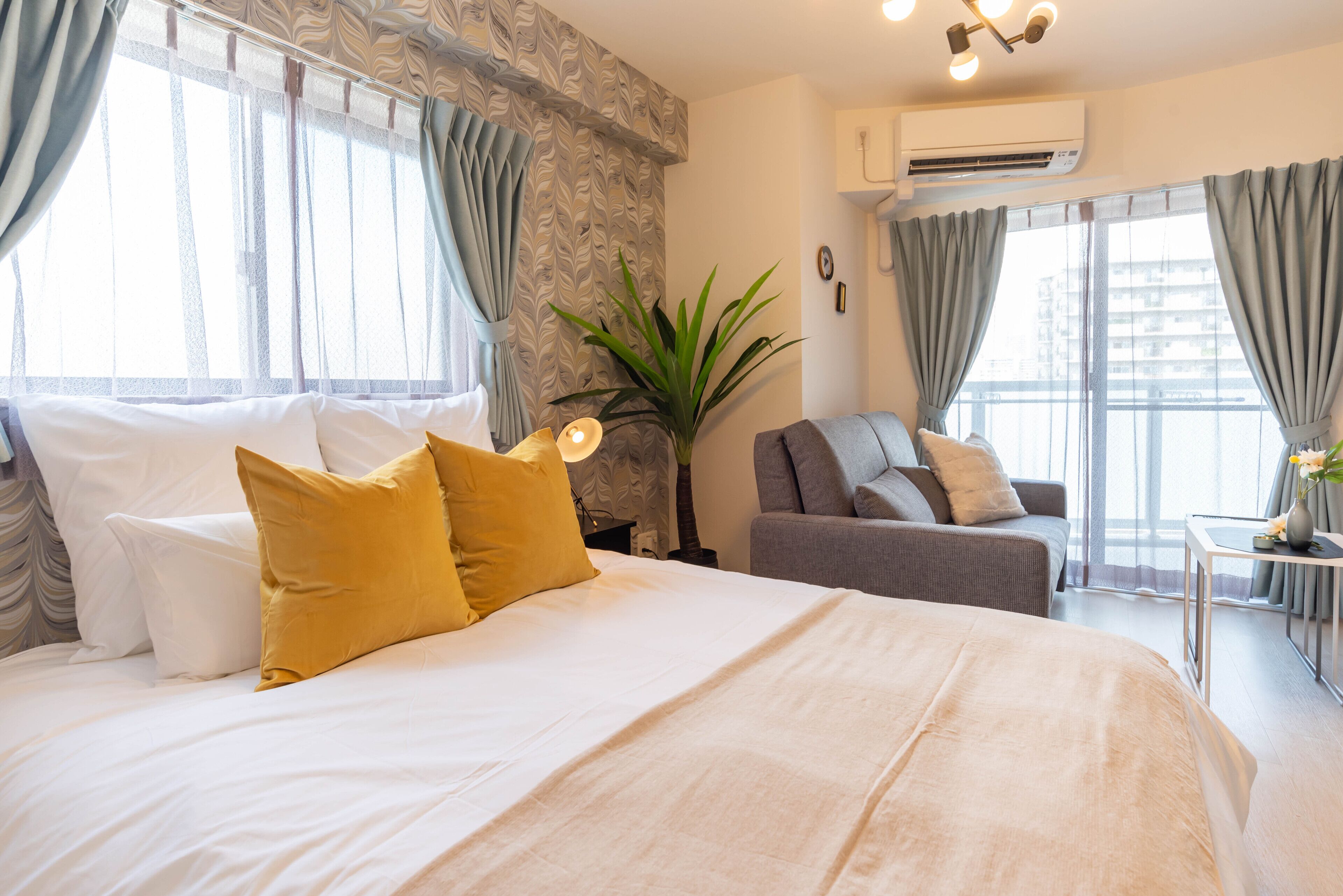 A hotel room with a large bed, a sofa, a potted plant, and a view of the city.