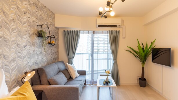 Ein modernes Hotelzimmer mit einer Couch, einem Bett, einem kleinen Tisch mit einer Vase, einer Topfpflanze und einem an der Wand befestigten Fernseher.
